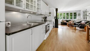 A modern kitchen with white cabinets, a black countertop, and a stove. There is a dining area with a black leather couch and a coffee table.