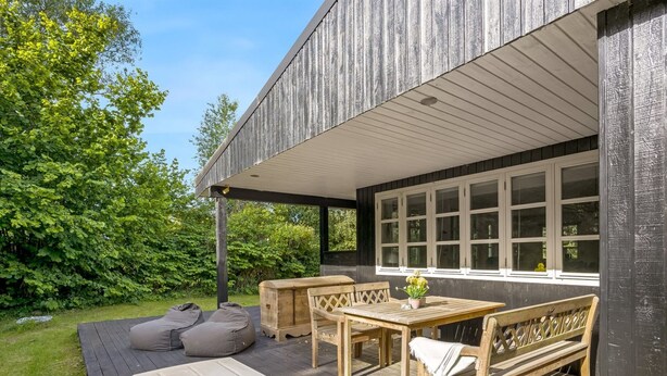 A wooden deck with a table and benches, surrounded by greenery.