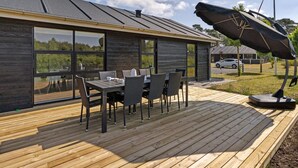 Een modern huis met terras, grote ramen en een eethoek met tuinmeubilair.