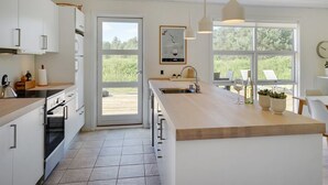 Een moderne keuken met witte kastjes, een groot eiland en een uitzicht op het omliggende landschap door grote ramen.