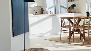 Een moderne keuken met witte kasten, een houten eettafel en een geweven zitkussen.