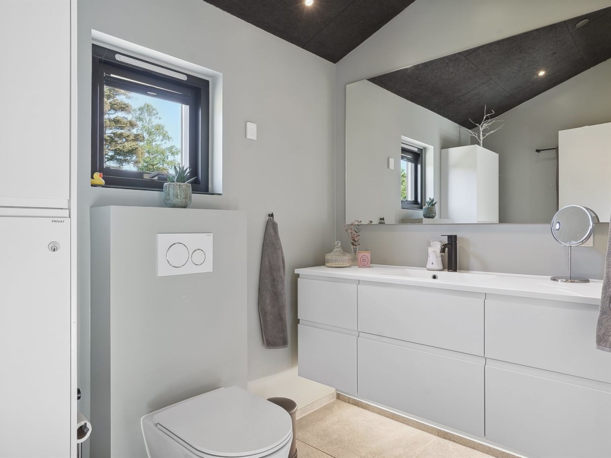 Une salle de bain moderne avec des toilettes, un lavabo et un miroir. Il y a une fenêtre au-dessus du lavabo, et une serviette est accrochée au mur.