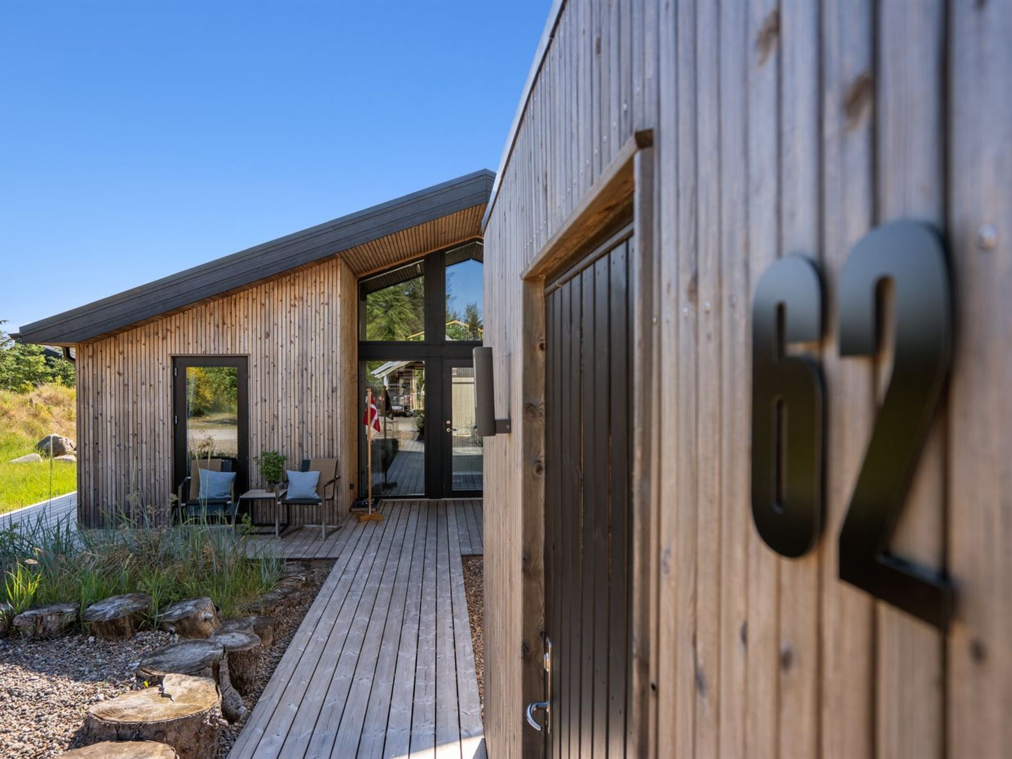 A wooden cabin with a deck, a door marked with the number 62, and a patio area with outdoor furniture.