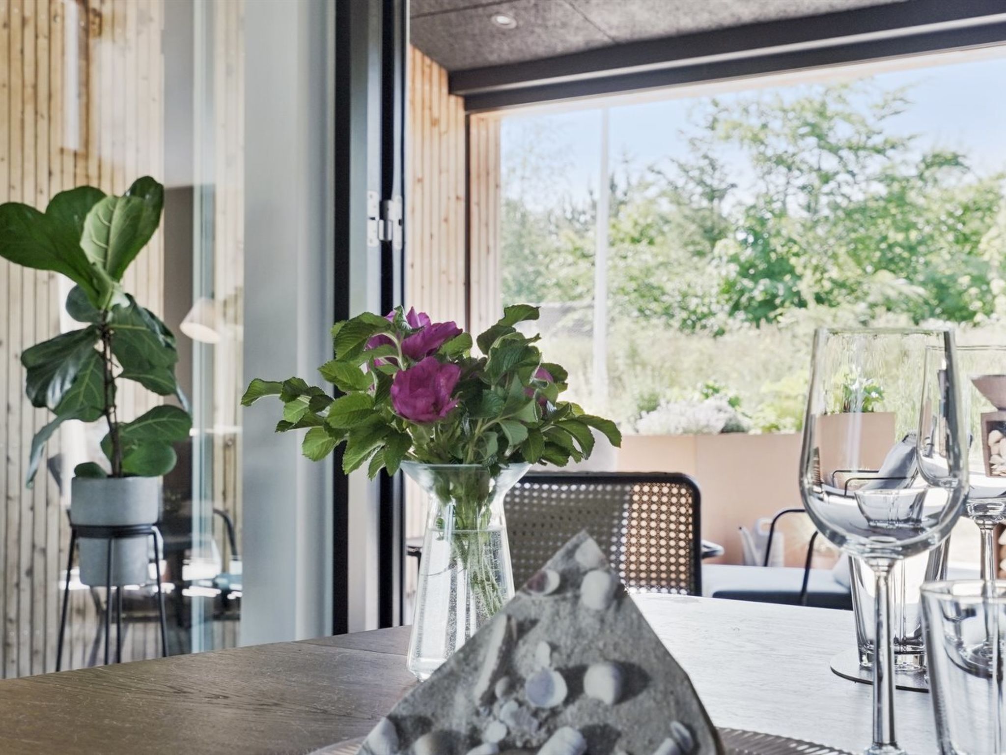 A dining table with a clear view of the outdoors, a potted plant, and a vase with flowers.