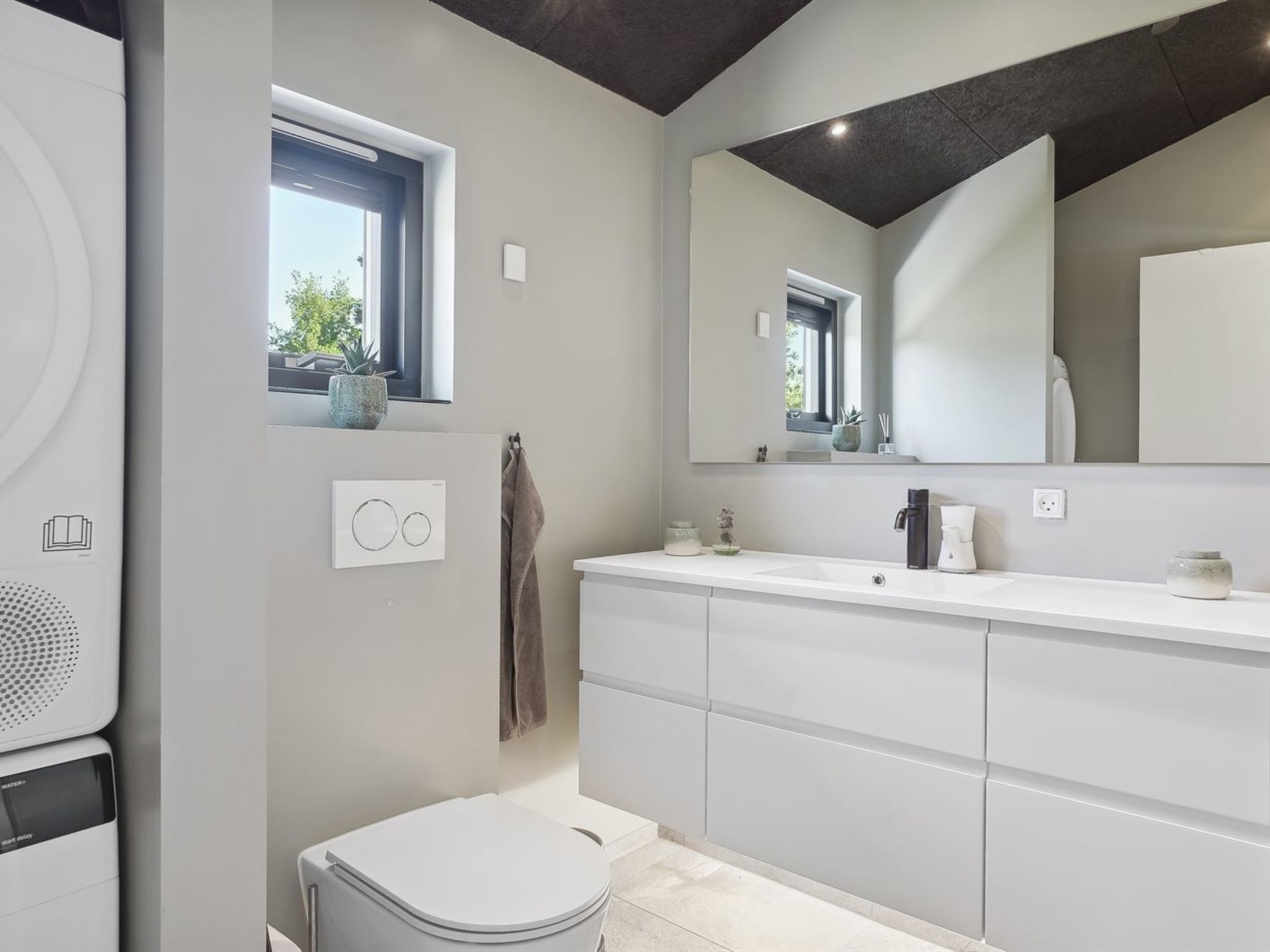 A modern bathroom with a large mirror, white vanity, and a toilet.