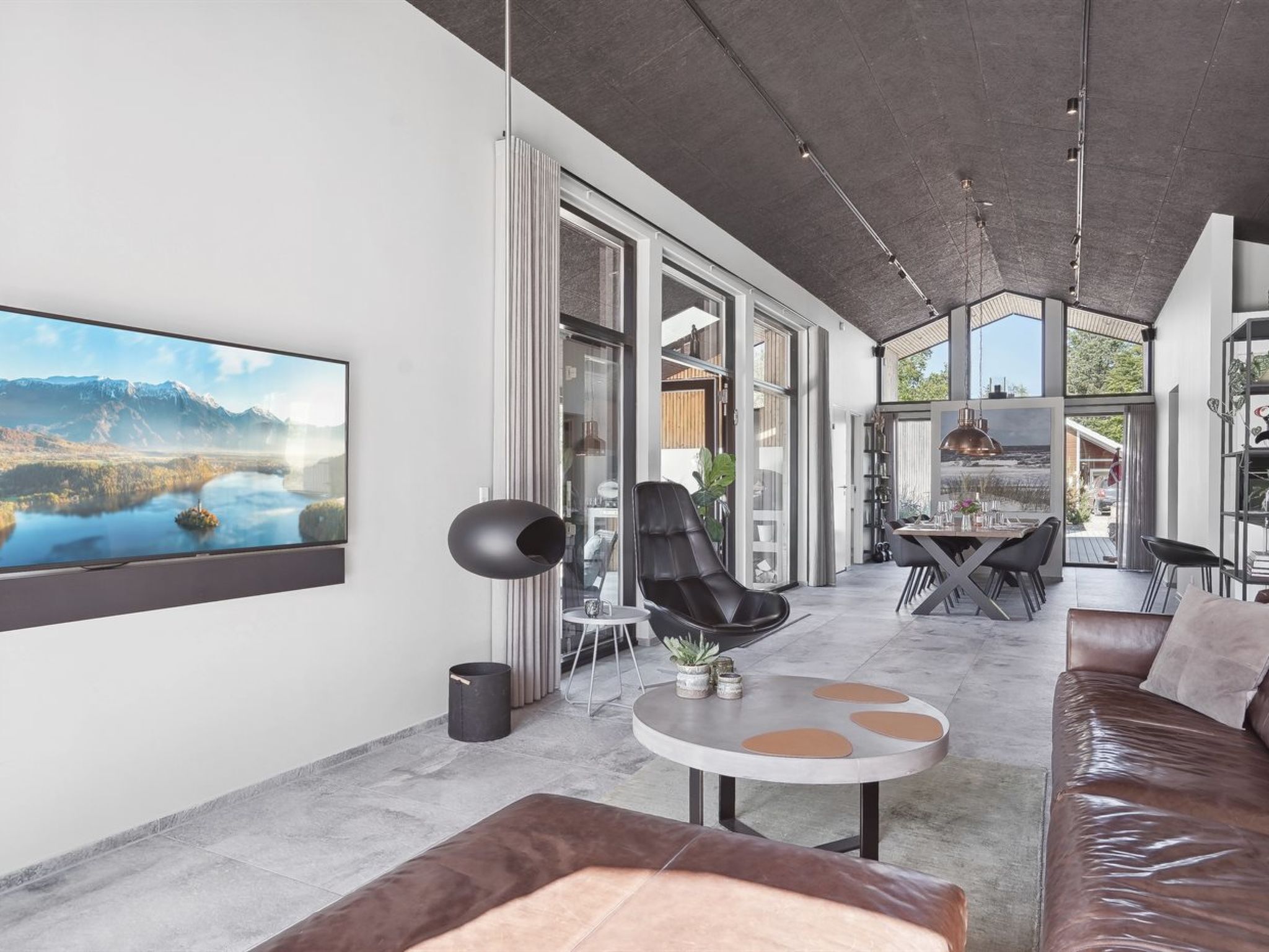 Ein modernes Wohnzimmer mit großem Fenster, einem schwarzen Sessel, einem runden Tisch und einem Ledersofa.