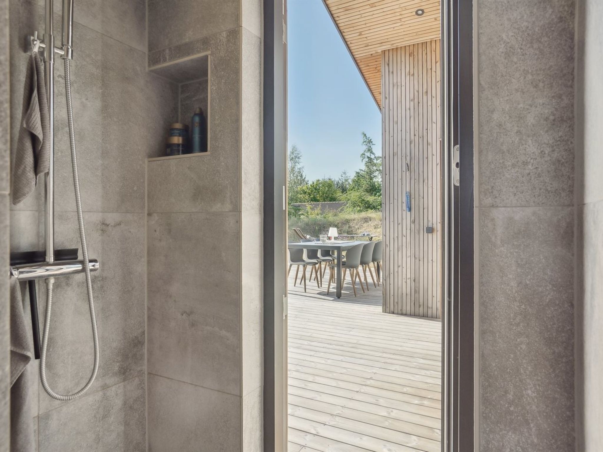 Chuveiro moderno com porta de vidro, deck de madeira e vista para uma área de estar externa.