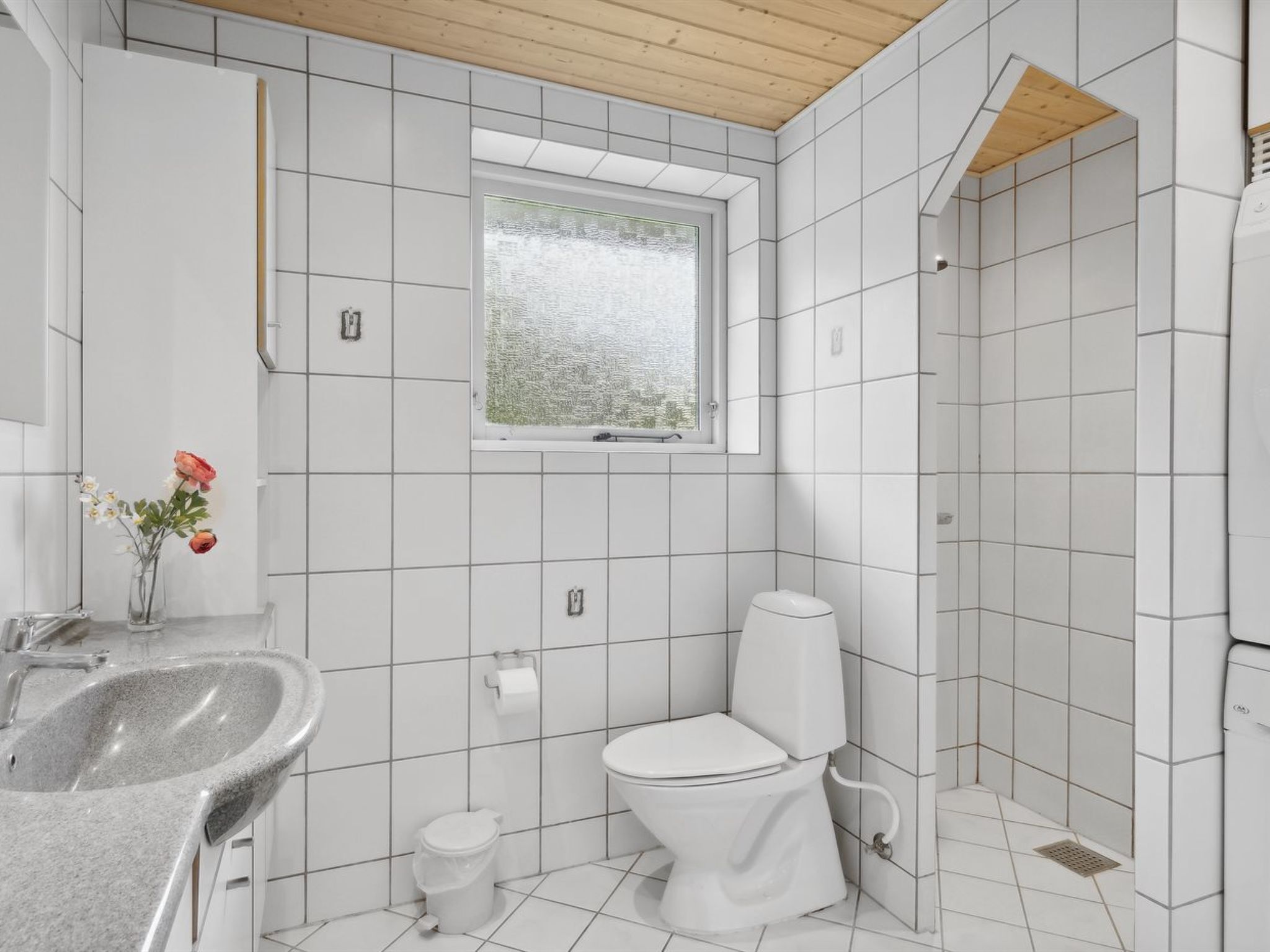 A modern bathroom with white tiles, a granite sink, a toilet, and a shower area.