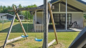 A wooden swing set in a backyard with a covered patio area and a brick house in the background. - "Henny" - 1.5km from the sea by Interhome (Hals)
