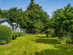A residential property with a well-maintained lawn, a house with a blue roof, and dense surrounding trees.