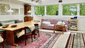 A room with a wooden dining table, chairs, a sofa, a small side table, and a window with a view of greenery. - "Lenard" - 400m from the sea by Interhome (Hals)