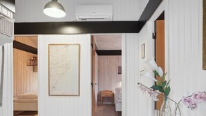 A hallway with white walls, a wooden floor, and a black ceiling. There is a framed map on the wall, a vase with flowers, and a door leading to another room.