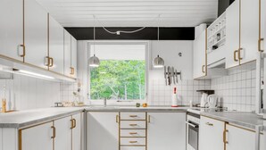 A modern kitchen with white cabinets, wooden handles, a central island with a sink, and a window with a view of greenery.