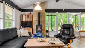 A cozy living room with a black leather sofa, a wooden coffee table, and a black leather armchair. A television is mounted on the wall, and a fireplace is visible in the background.