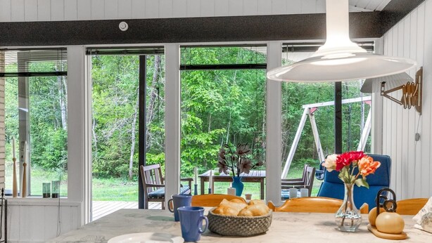 A dining area with a table set for four, large windows, and a view of greenery outside.