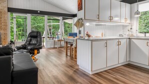 A modern kitchen with white cabinetry, a dining area with a black leather chair, and large windows offering a view of greenery.