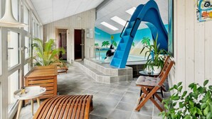 Ein moderner Poolbereich im Innenbereich mit einer blauen Rutsche, Sitzgelegenheiten und Topfpflanzen.
