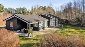 Une cabane moderne à deux étages, dotée d’un patio couvert et d’un garage, et entourée d’un paysage boisé.
