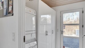 Une buanderie équipée d’une machine à laver et d’un sèche-linge superposés, une porte avec une fenêtre et un tableau d’affichage fixé au mur.