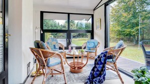 A sunlit room with wicker chairs, a small table, and a large window offering a view of a garden.