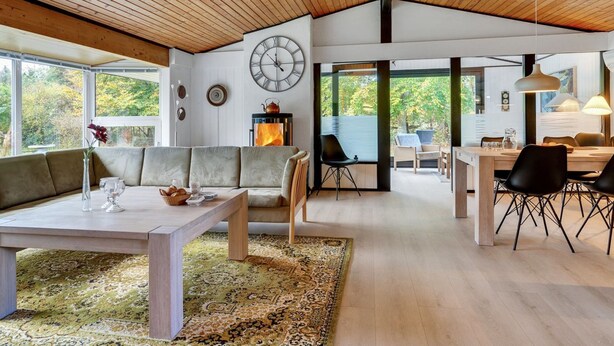 A spacious living area with a wooden ceiling, a large clock, and a fireplace.