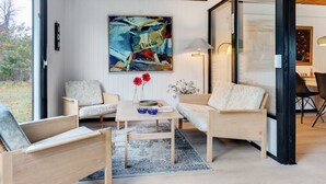 A modern living room with a large window, a painting, and a dining area.
