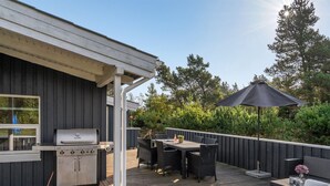 An outdoor deck with a grill, dining table, chairs, and an umbrella.