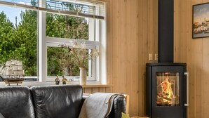 A cozy living room with a black leather sofa, a fireplace, and a window with a view of trees.