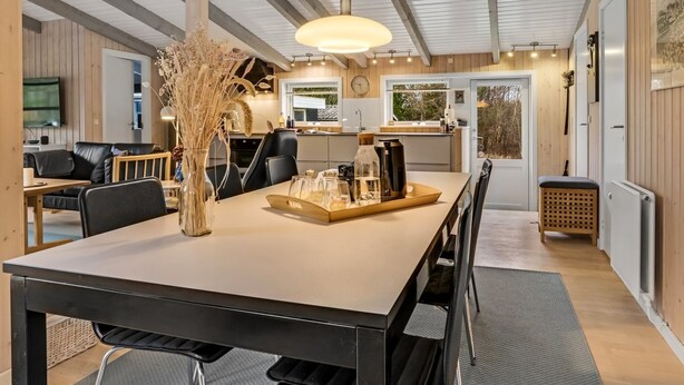 A modern kitchen with a dining area, wooden beams, a hanging light fixture, and a view of the outdoors.