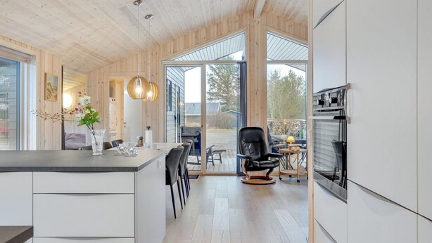 Een moderne keuken met houten plafond en grote ramen, een eetgedeelte met een zwarte stoel en uitzicht op de omgeving.