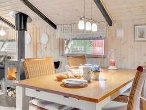 Un coin repas chaleureux avec une table en bois, des chaises en osier et un poêle à bois.