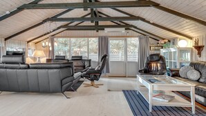 Een ruime woonkamer met een hoge plafond, een zwarte leren bank, een leren fauteuil, een salontafel en een boekenkast.