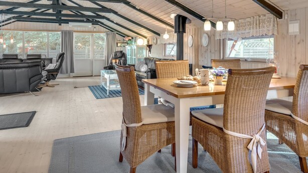 Een ruime woonkamer met een eettafel, rieten stoelen, een leren bank en een groot raam voor natuurlijk licht.