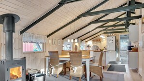 Een gezellig chaletinterieur met een houtkachel, een eethoek met rieten stoelen en een keuken met een koelkast.