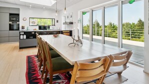 Et moderne køkken med spiseplads, store vinduer og udsigt til grønne omgivelser.