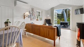 En moderne stue med en træbænk, et spisebord med stole, en pejs og udsigt til naturen.