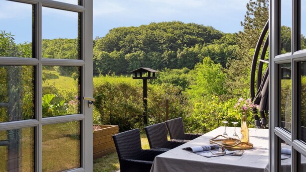 En åben terrasse med et spisebord, med udsigt over et frodigt grønt landskab og en bakke.