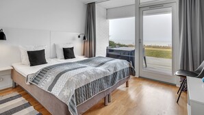 Une chambre moderne avec un grand lit, un bureau et une vue sur la mer, accessible par une porte-fenêtre coulissante.