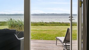 Vue depuis une pièce dont la porte est en verre et qui donne sur une terrasse surplombant un lac.