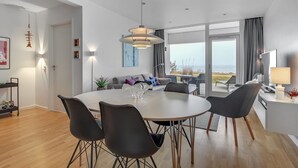 Un espace repas moderne avec une table ronde, des chaises noires et une grande fenêtre donnant sur la mer.