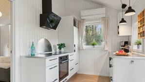 A modern kitchen with white cabinetry, a built-in oven, a sink, and a window with curtains. - "Etel" - 600m from the sea by Interhome (Ebeltoft)