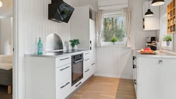 Moderni keittiö, jossa on valkoiset kaapit, sisäänrakennettu uuni, pesuallas ja ikkuna, jossa on verhot.