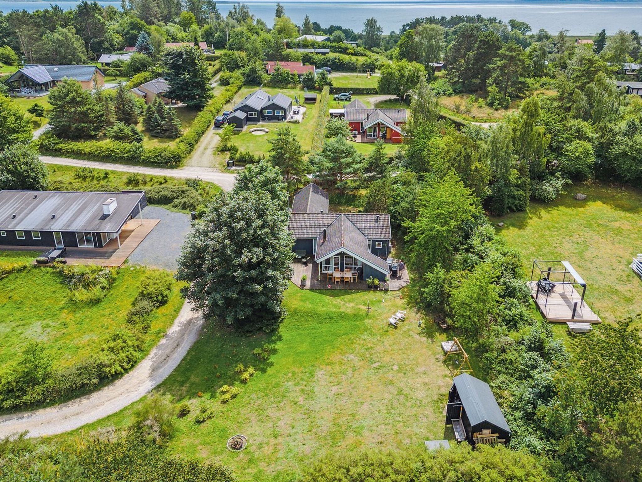 Vue aérienne d’un quartier résidentiel avec des maisons, un grand arbre et une étendue d’eau en arrière-plan.