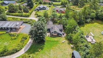 Ovenudtagning af et boligområde med huse, et stort træ og et vandareal i baggrunden.