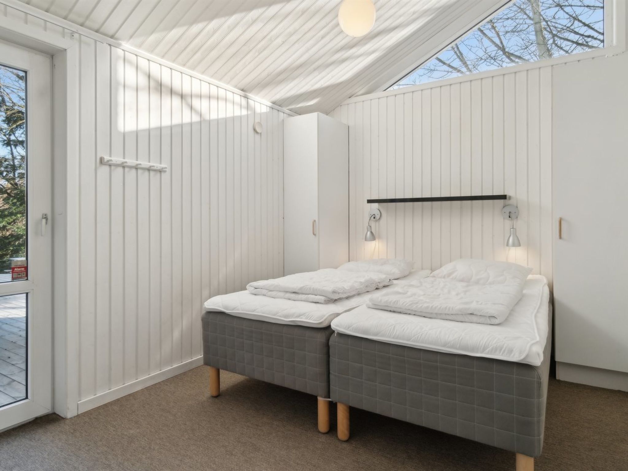 A modern bedroom with a large bed, a skylight, and a white exterior wall.