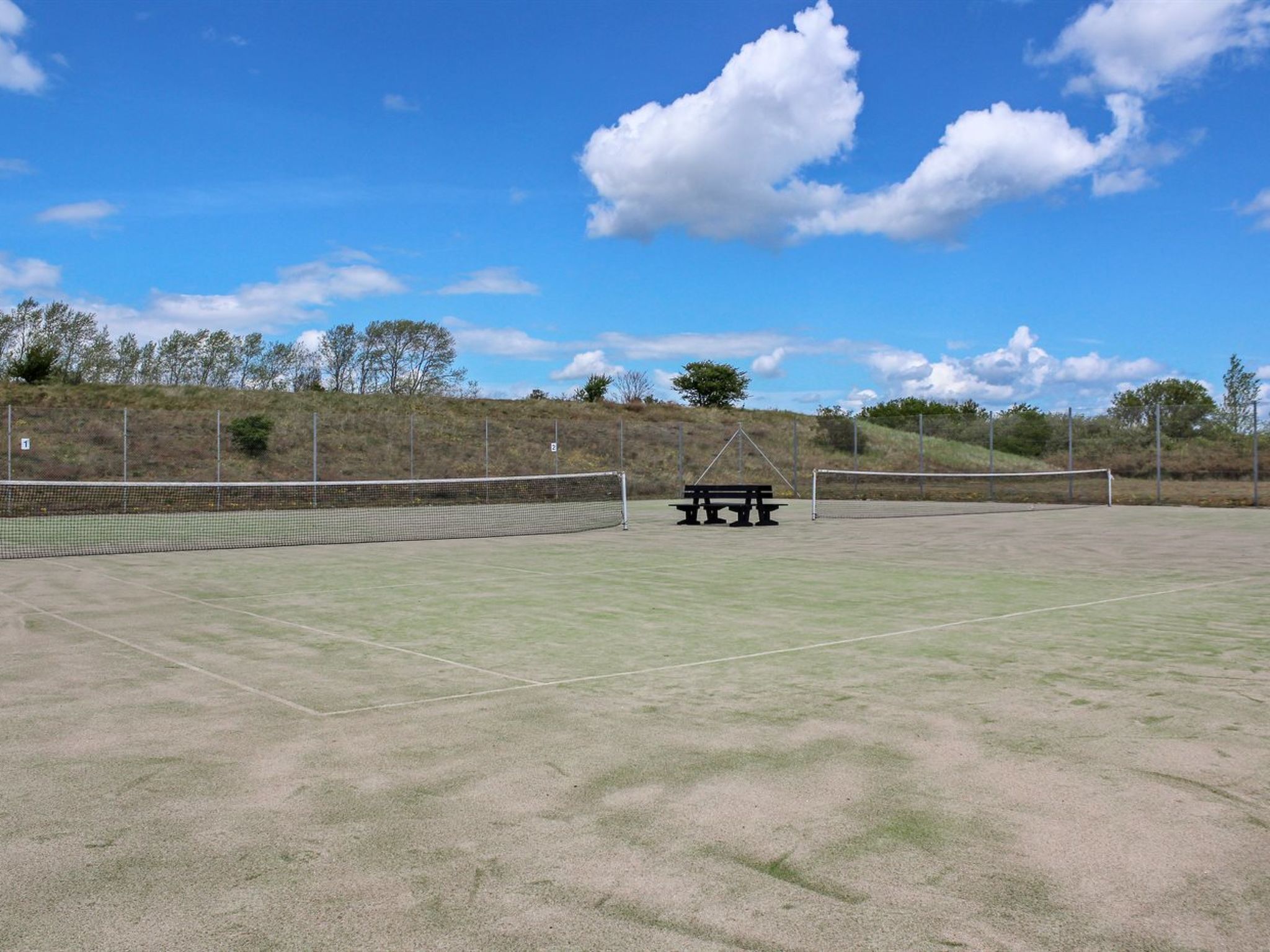 Una cancha de tenis al aire libre con una mesa de picnic y una red.