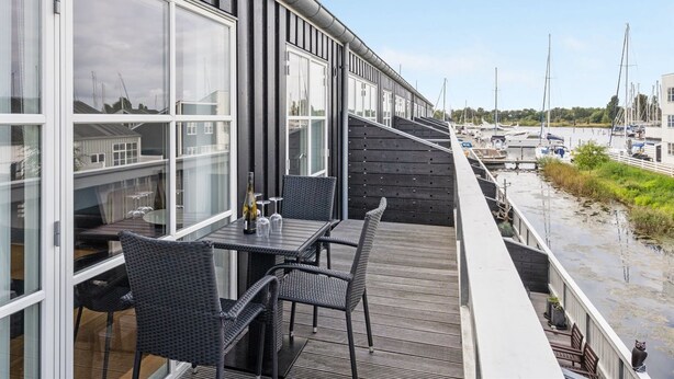 Una terraza moderna al aire libre con una mesa y sillas, con vistas a un puerto deportivo lleno de barcos.