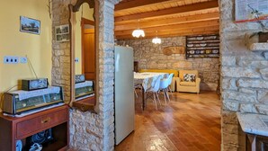 A rustic interior with stone walls, a wooden ceiling, a dining area with a table and chairs, and a vintage radio on a wooden cabinet.