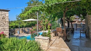 A pool area with a stone wall, lounge chairs, and a pergola with vines.
