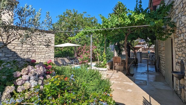 A stone-walled courtyard with a garden, outdoor seating, and a pergola.